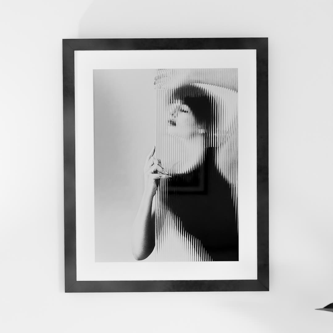 Emergence, framed with a white mat on a white wall: a woman with closed eyes, her face and raised hand rising out of vertical bands of refraction